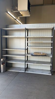 des étagères dans un garage, avec une poubelle et une autre poubelle à l'arrière-plan