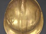 brass plated helmet on a black surface with a black background