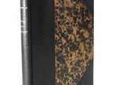 an old book with a black cover sitting on a white surface