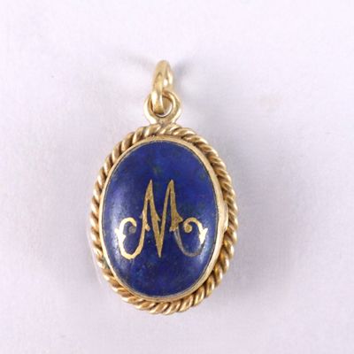 un gros plan d'un pendentif en or et lapis-lazuli orné d'une lettre « m »