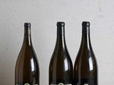 trois bouteilles de vin posées sur une table en bois, à côté d'une bouteille de vin