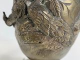 a silver vase with a bird on it sitting on a table