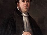 portrait of a man in a black coat and white shirt holding a book