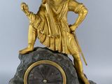 gold statue of a man sitting on top of a rock with a clock in front of him