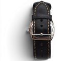 bracelet de montre en cuir noir avec des surpiqûres dorées sur fond blanc