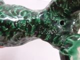 a hand holding a green dog statue on a tile floor