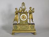 a gold clock with three girls on it and a bird in the middle