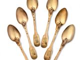 six cuillères en or sont disposées en cercle sur une surface blanche
