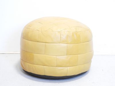 yellow leather pouffe sitting on a white floor in front of a white wall