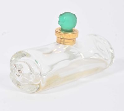 une petite bouteille en verre avec un bouchon vert posée sur une surface blanche