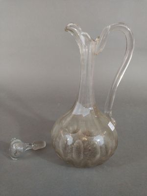 a clear glass pitcher with a handle and a glass stopper next to it