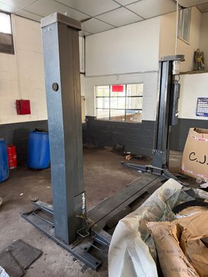 une photo d'un garage avec un grand pont élévateur au milieu de la pièce