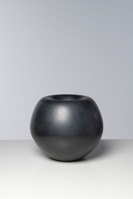 un vase noir posé sur une table près d'un mur blanc