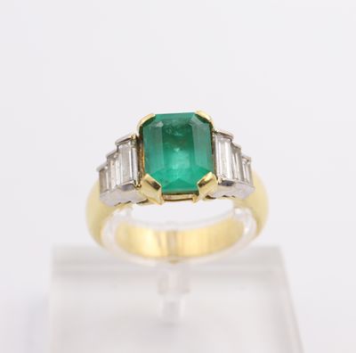 an emerald and diamond ring on display on a clear surface