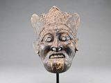 sculpture représentant le visage d'un homme, posée sur un socle, avec un fond gris