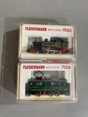 une paire de deux trains miniatures dans des boîtes en plastique, posés sur une surface blanche