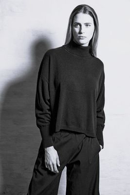 a black and white photo of a woman in a turtle neck sweater and wide legged pants