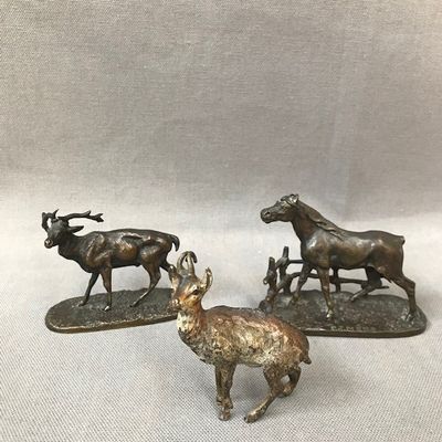 two bronze statues of animals and a goat on a white surface