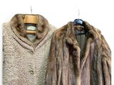 pair of fur coats on hangers against a white wall