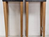 pair of wooden stools with black seat cushions against a white wall
