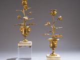 pair of gold vases with flowers on marble bases against a gray background