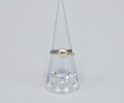 une bague ornée d'une perle, posée sur un cône transparent