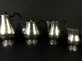 three silver coffee pots and two silver cups on a black surface