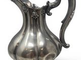 a silver pitcher on a stand on a white surface