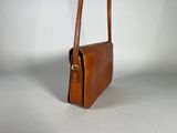 the small brown leather bag is sitting on a white surface
