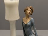 une figurine représentant une femme assise sur une table, à côté d'une lampe