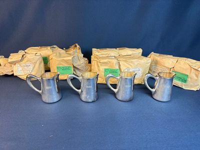 six silver mugs with labels on them sitting on a blue surface