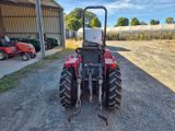 a red tractor parked in front of a building on a dirt road