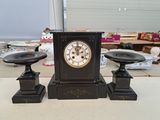 une horloge noire posée sur une table, à côté de deux bougies