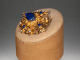an image of a gold ring with blue stones on top of a wooden box