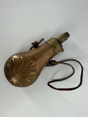 un petit objet en laiton posé sur une surface blanche, muni d'un cordon marron