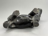 une sculpture noire représentant un chien couché sur le dos