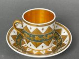 cup and saucer decorated with gold and green designs on a gray surface