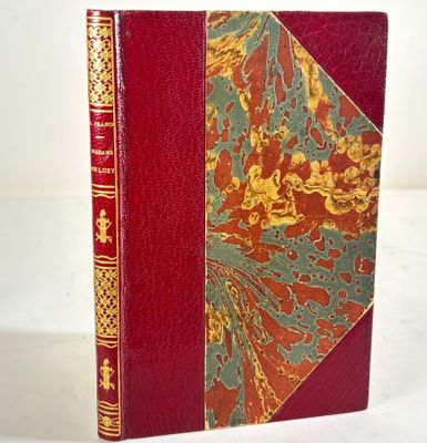 an old book with a red cover and gold trim on a white surface