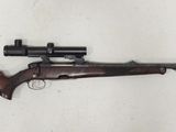 Un vieux fusil repose sur une surface blanche ; il est équipé d'une lunette de visée.