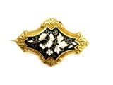 une image représentant une broche noire et dorée ornée de fleurs blanches