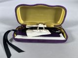 glasses in a purple case on a white surface with a black ribbon