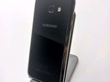 a black samsung phone sitting on a stand on a white surface