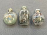 trois flacons à tabac en verre décorés de peintures, posés sur une table