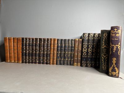 Plusieurs vieux livres sont alignés sur une étagère devant un mur gris.