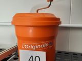 un gobelet orange muni d'un couvercle et d'une anse, posé sur une étagère