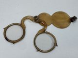 une paire de lunettes anciennes en laiton posée sur une surface blanche