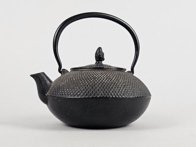 une théière noire avec une anse, posée sur un fond blanc