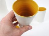 a person holding a yellow and white cup in their hand