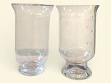 une paire de vases en verre transparent posés sur une surface blanche