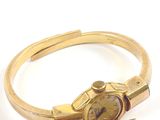 bracelet en or jaune avec une montre posée sur le côté, sur un fond blanc
